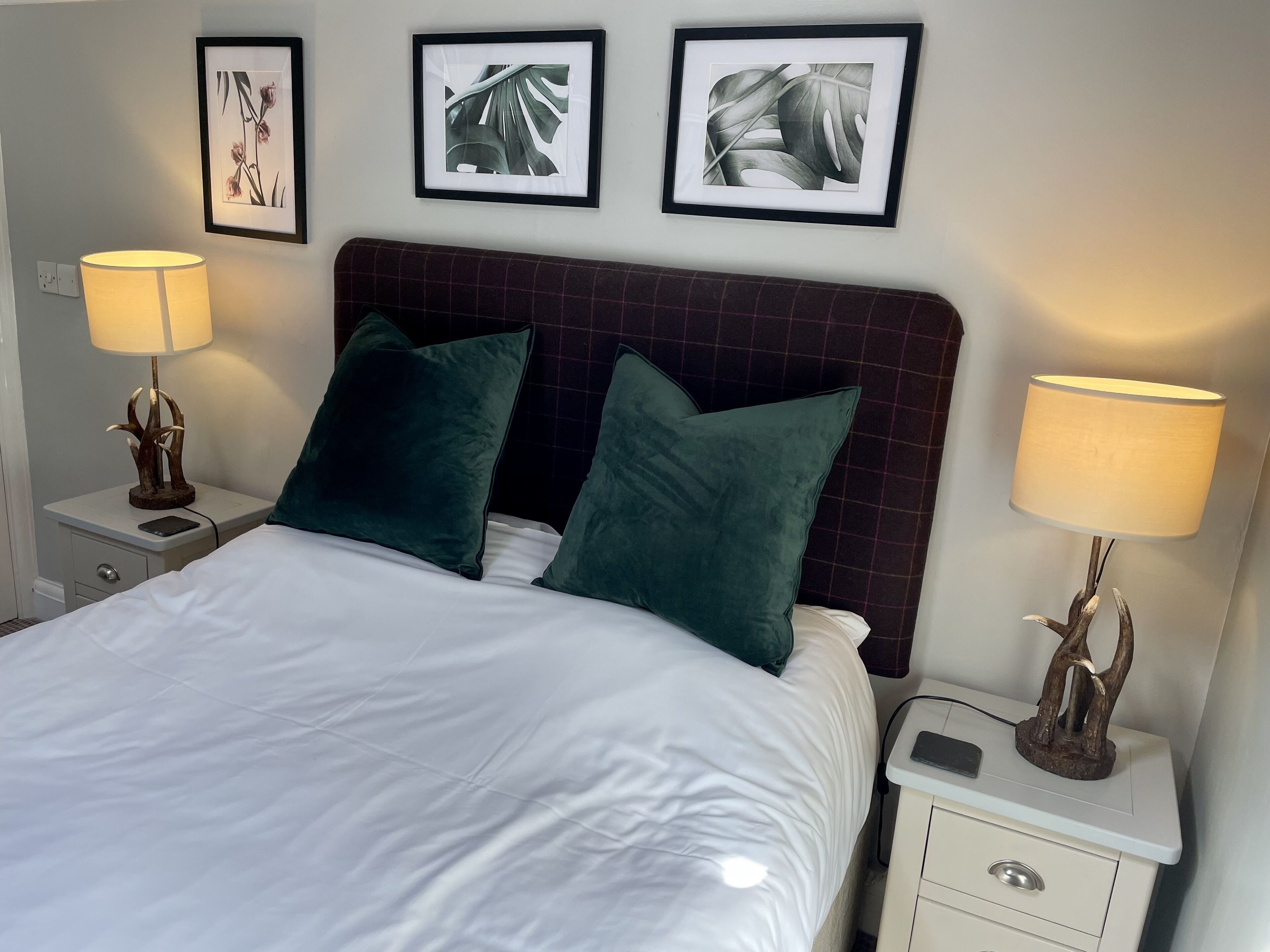 A neatly made bed with two green pillows, a headboard, and two bedside lamps. There are framed pictures on the wall above the bed.