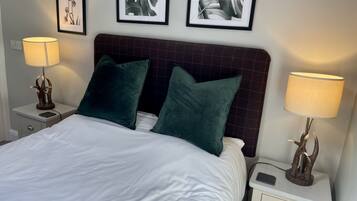 A neatly made bed with two green pillows, a headboard, and two bedside lamps. There are framed pictures on the wall above the bed.