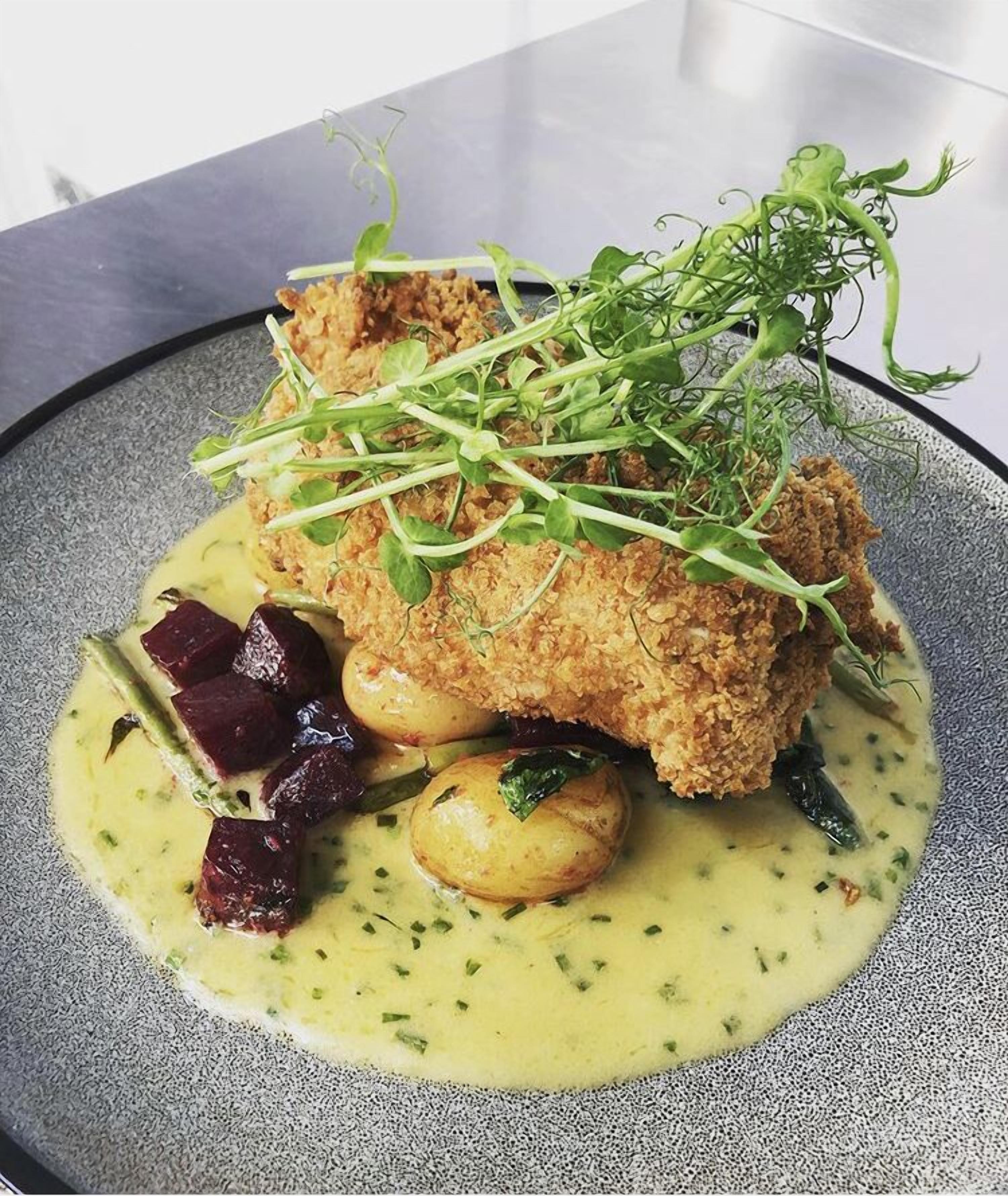 A plate with a breaded item, potatoes, and greens on a speckled plate.