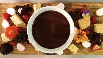 Una taza de chocolate rodeada de varios pasteles y frutas sobre una tabla de madera.