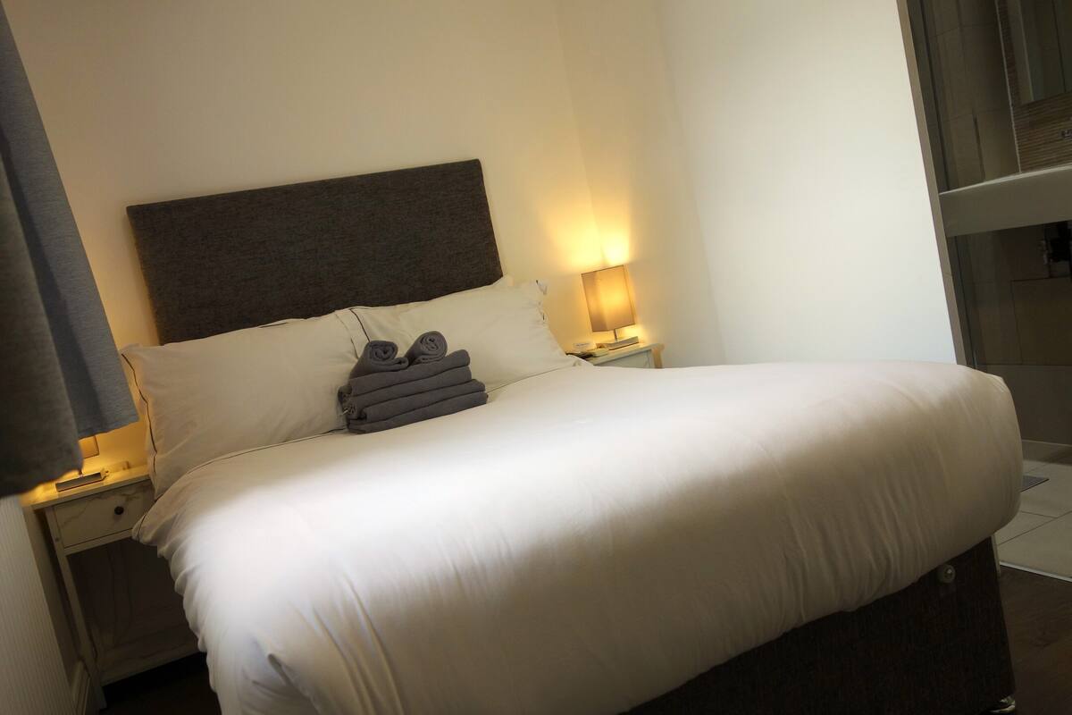 A neatly made bed with white linens, a dark headboard, and two bedside lamps.