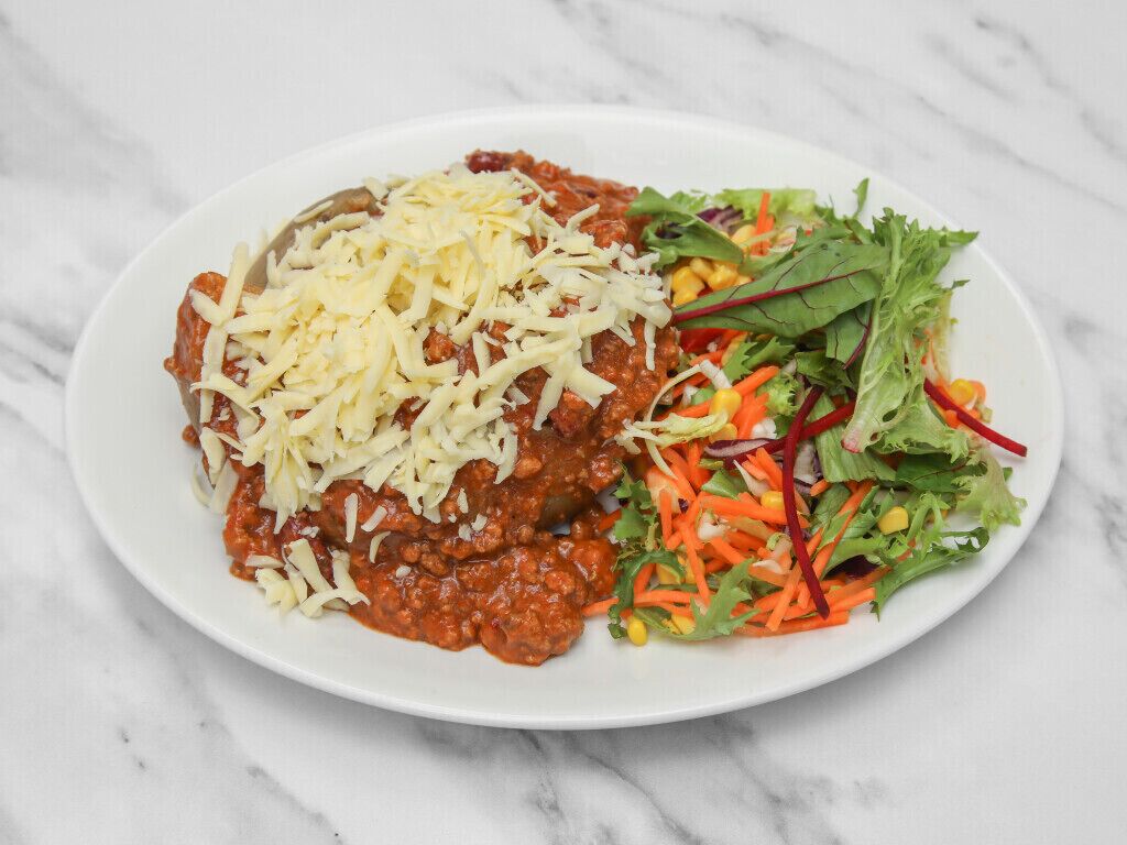 Une assiette contenant un plat de viande nappé de fromage, une salade en accompagnement et une sauce crémeuse.