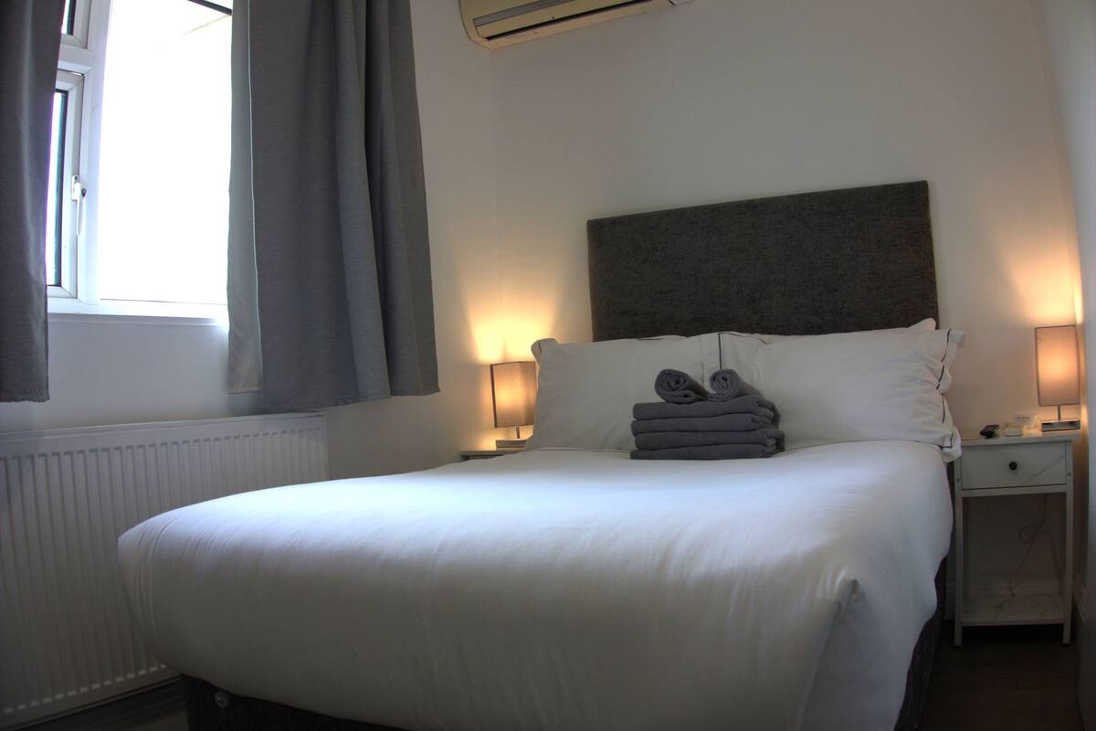A neatly made bed with white linens, a headboard, and a nightstand with a lamp.