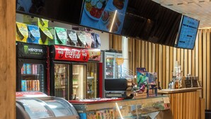 Un patio de comidas con máquinas expendedoras, un refrigerador de Coca-Cola y una vitrina con pasteles.