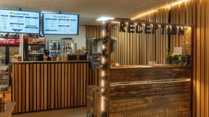 Un mostrador de recepción con detalles de madera y un letrero que dice "RECEPTION". Encima del mostrador hay dos paneles con la carta del almuerzo.