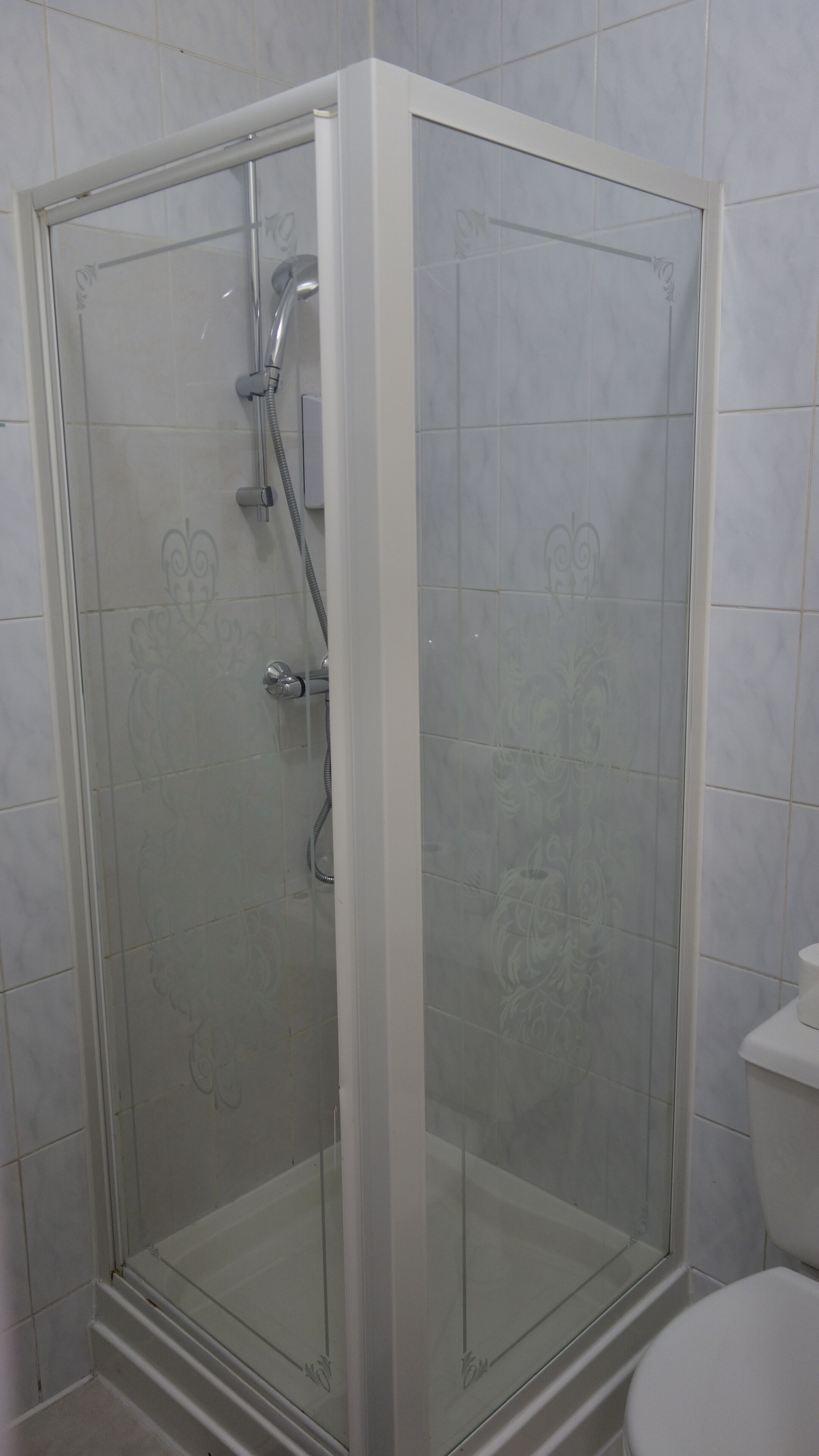 A glass-enclosed shower with a handheld showerhead and a wall-mounted faucet.