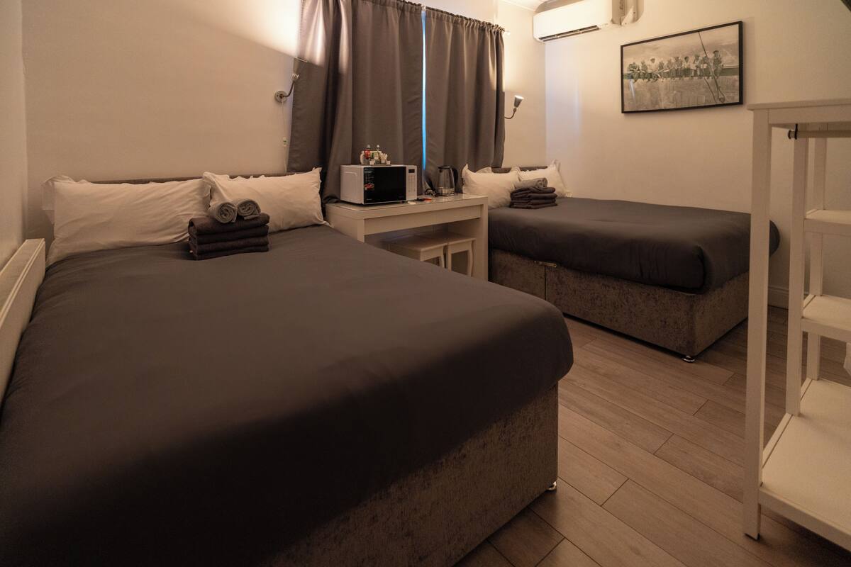 A hotel room with two beds, a small table with a microwave, and a framed picture on the wall.