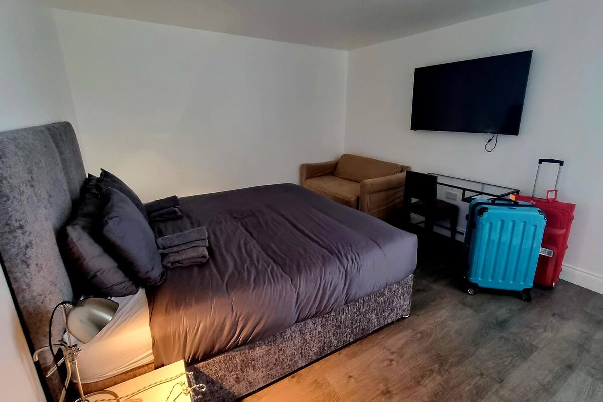 A hotel room with a bed, a desk, a chair, a television, and a suitcase.