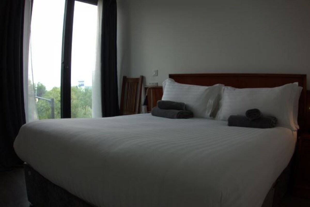 Habitación de hotel con una cama grande, cabecero de madera y vistas a zonas verdes.
