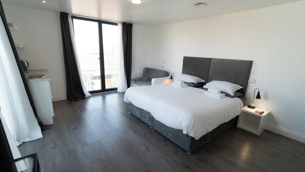 Habitación de hotel moderna con una cama grande, una mesita de noche, un escritorio pequeño y vistas al exterior a través de una puerta corredera.