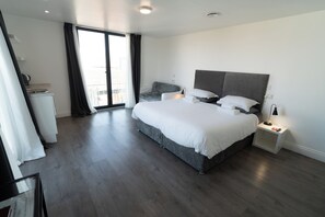 A modern hotel room with a large bed, a bedside table, a small desk, and a view of the outdoors through a sliding door. -  Abbey Point Hotel (London)