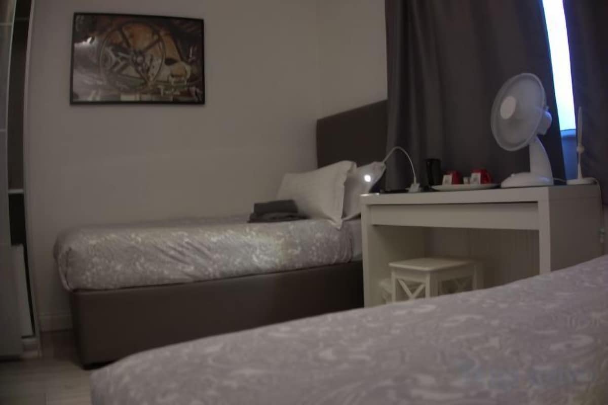 A bedroom with a bed, a desk, a chair, a lamp, and a painting on the wall.