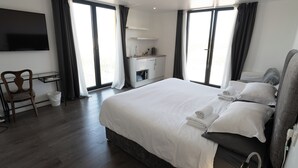 Una habitación de hotel moderna con una cama grande, un escritorio con silla, un televisor montado en la pared y vistas a través de las ventanas.