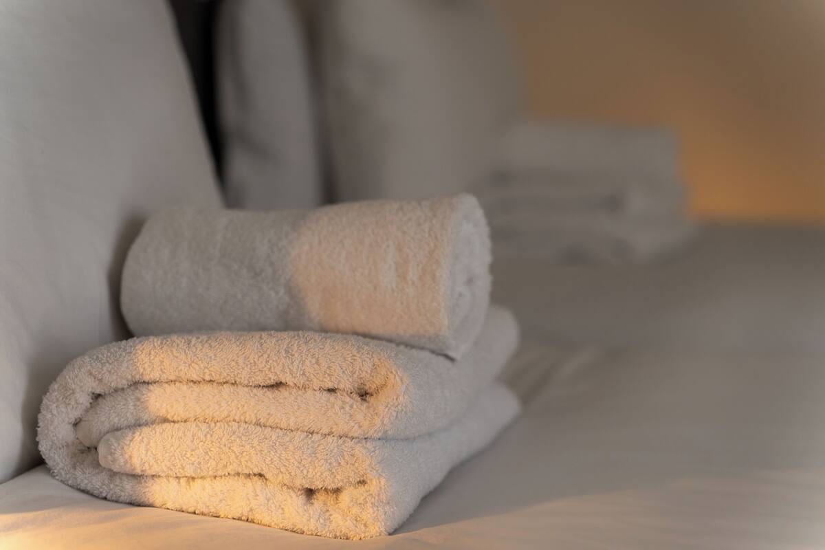 A neatly folded white towel on a bed with a pillow in the background.