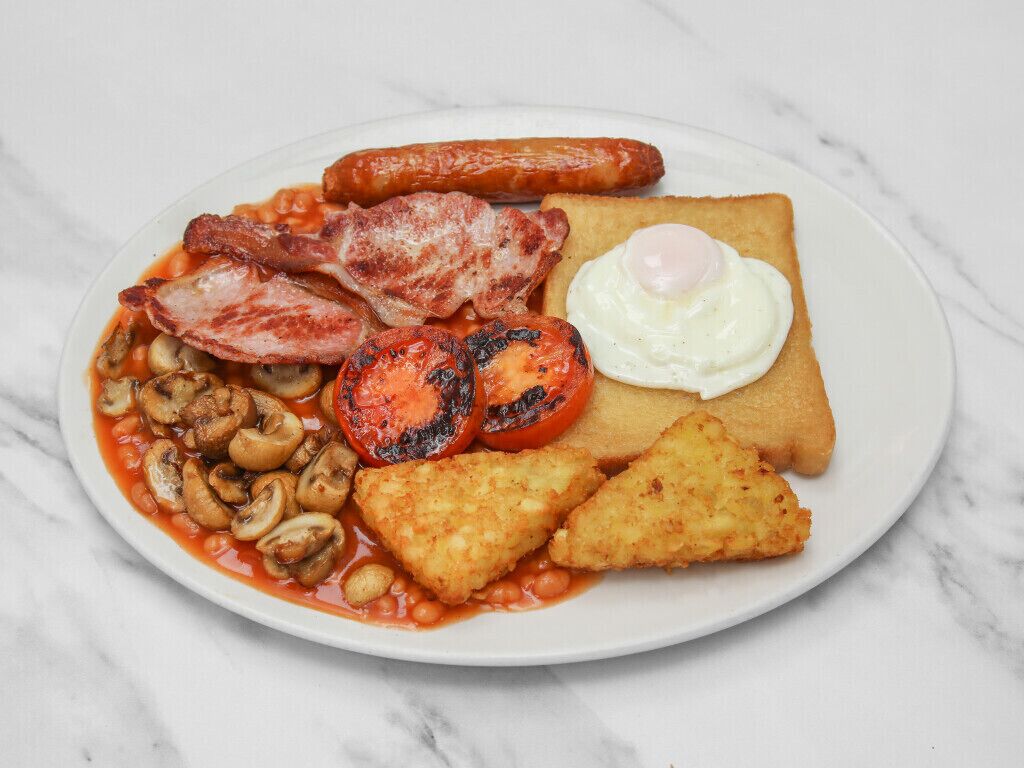 Un plato de comida para el desayuno con salchichas, tocino, champiñones, tomates, tostadas y un huevo frito.