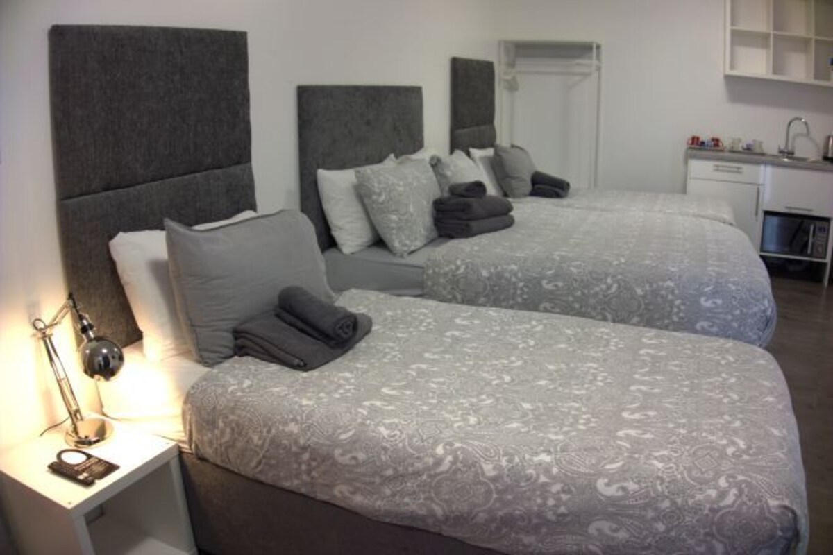 Una habitación de hotel con dos camas, un escritorio, una silla, una lámpara y un espejo.