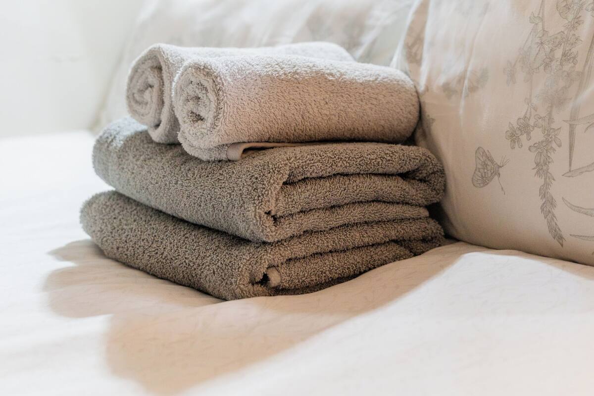 A neatly made bed with folded towels and a pillow with floral embroidery.