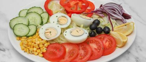 A plate of salad with cucumbers, tomatoes, boiled eggs, olives, and corn.