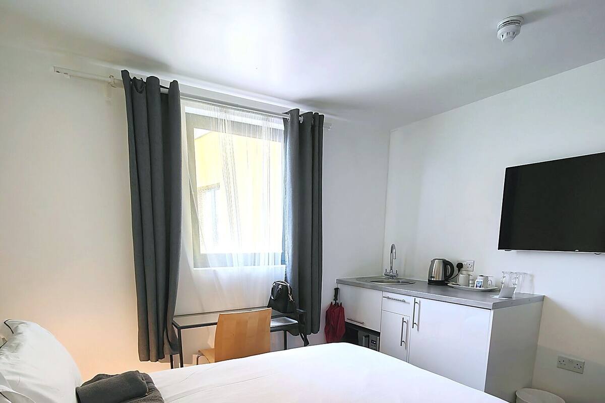 A hotel room with a bed, a desk, a chair, a TV, and a window with curtains.