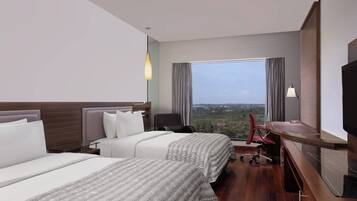 A hotel room with two beds, a desk, a chair, a TV, and a large window offering a city view.