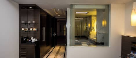 A modern hotel room with a large window, a walk-in closet, and a neatly arranged bathroom visible through the window.