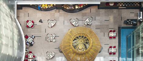 A top-down view of a hotel lobby with a central decorative structure, multiple seating areas, and a large window on the right.