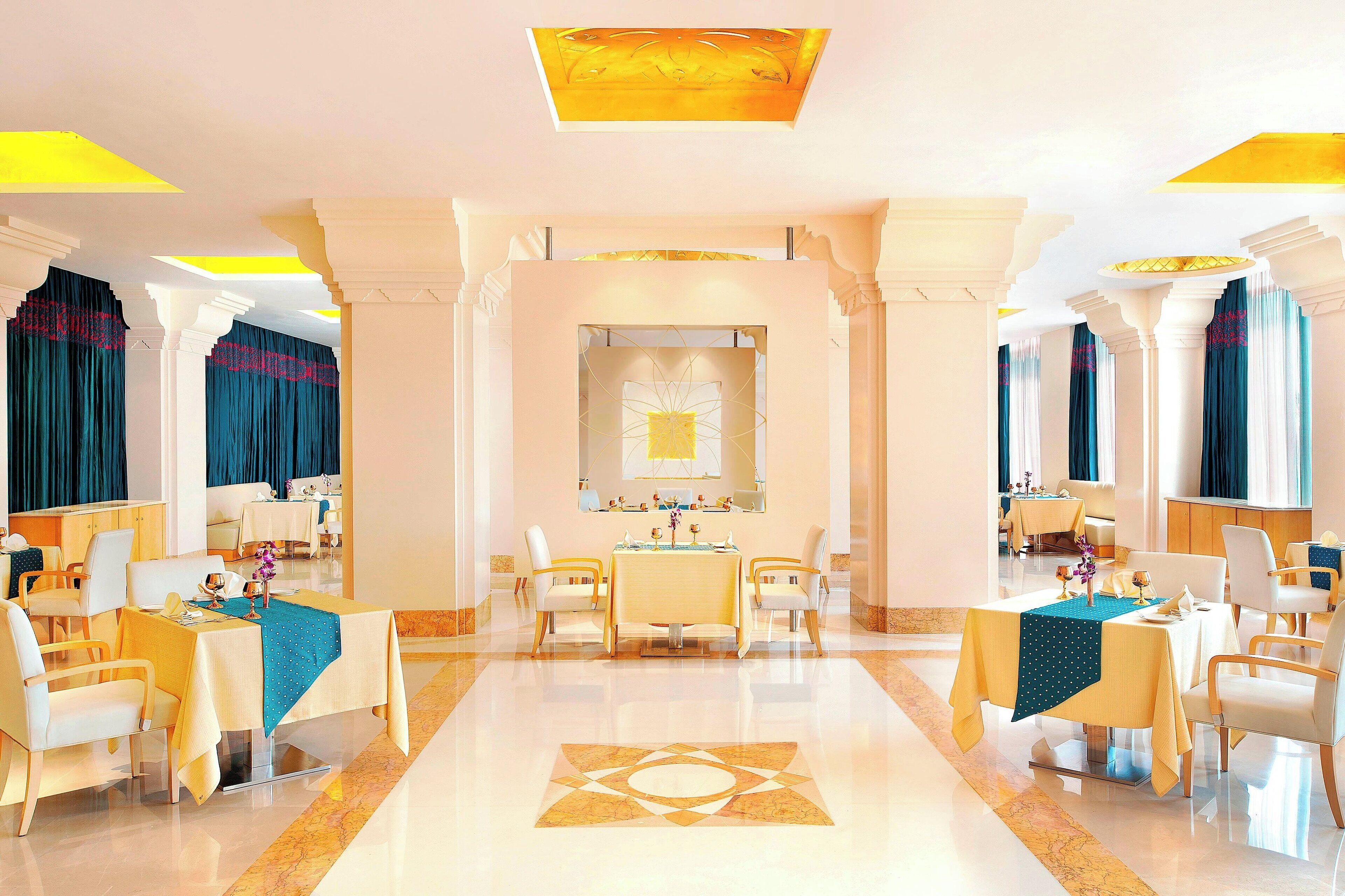 A hotel lobby with a central dining area, multiple seating arrangements, and a decorative floor pattern.