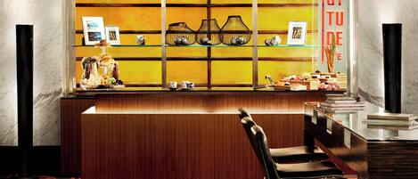 Una zona de bar con mostrador de madera, taburetes negros y estantes con diversos artículos.