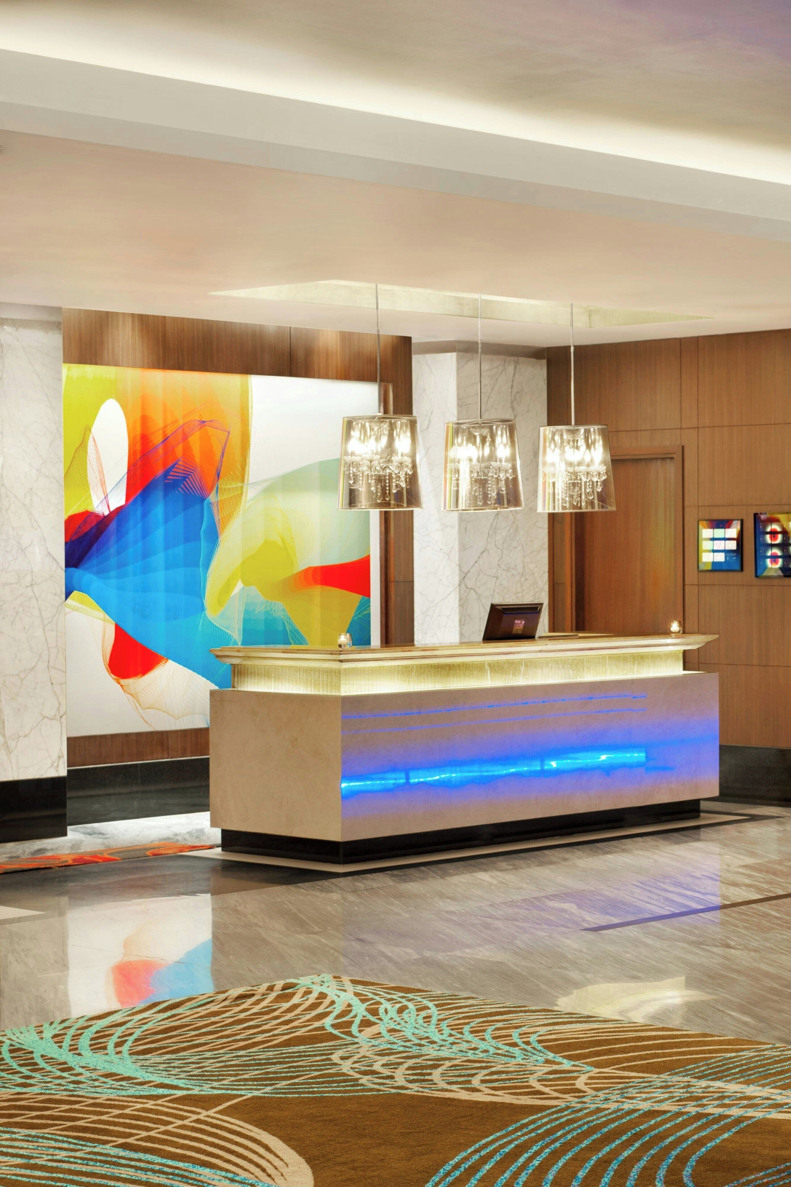 A hotel reception area with a modern design, featuring a reception desk, a colorful abstract mural, and a marble wall.