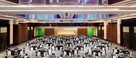 A large banquet hall with rows of round tables, each set with white chairs and black tablecloths.