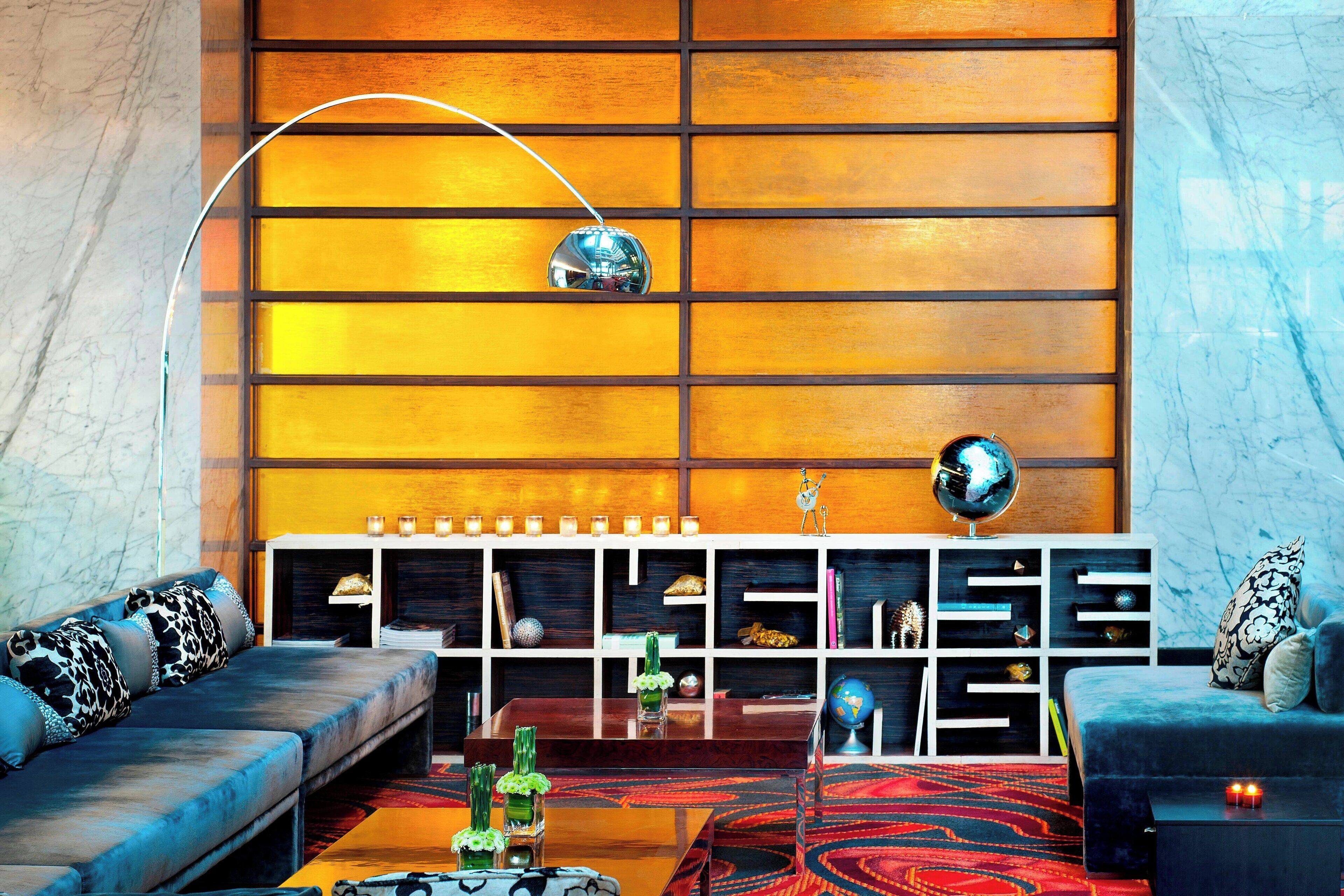 A modern living room with a sofa, a coffee table, and a patterned rug. There is a wooden wall with shelves and decorative items.