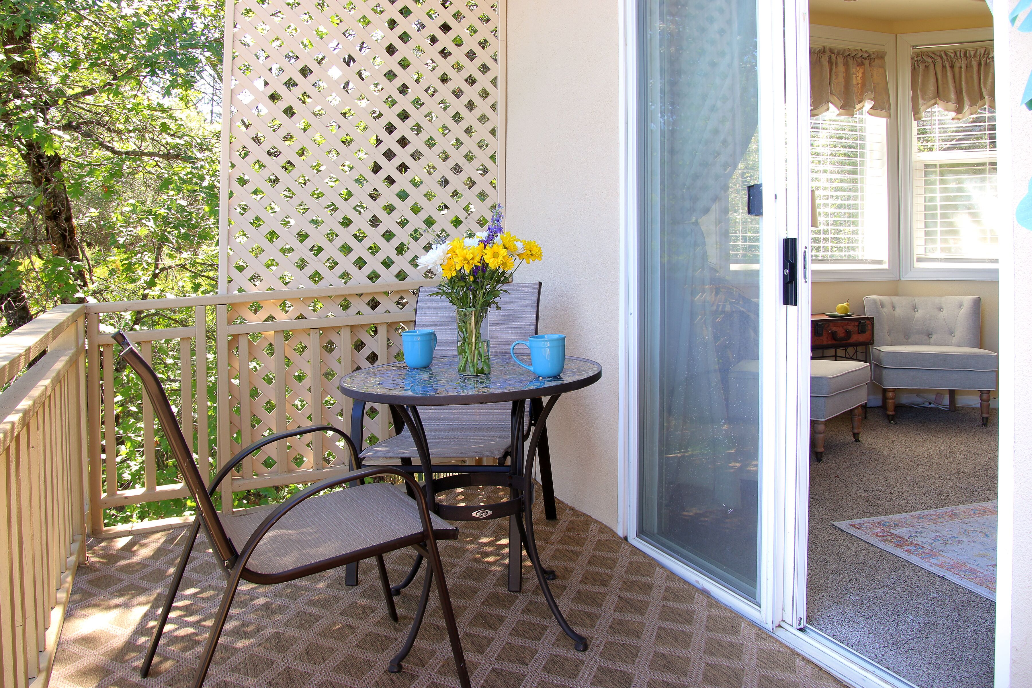 A balcony with a table, chairs, and a vase of flowers.