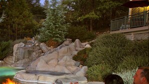 A couple relaxing by a fire pit with a rocky garden and a wooden deck in the background. - Bella Vista Bed and Breakfast (Placerville)