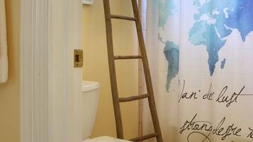 A bathroom with a toilet, a wooden ladder leaning against the wall, and a shower curtain with a world map design.