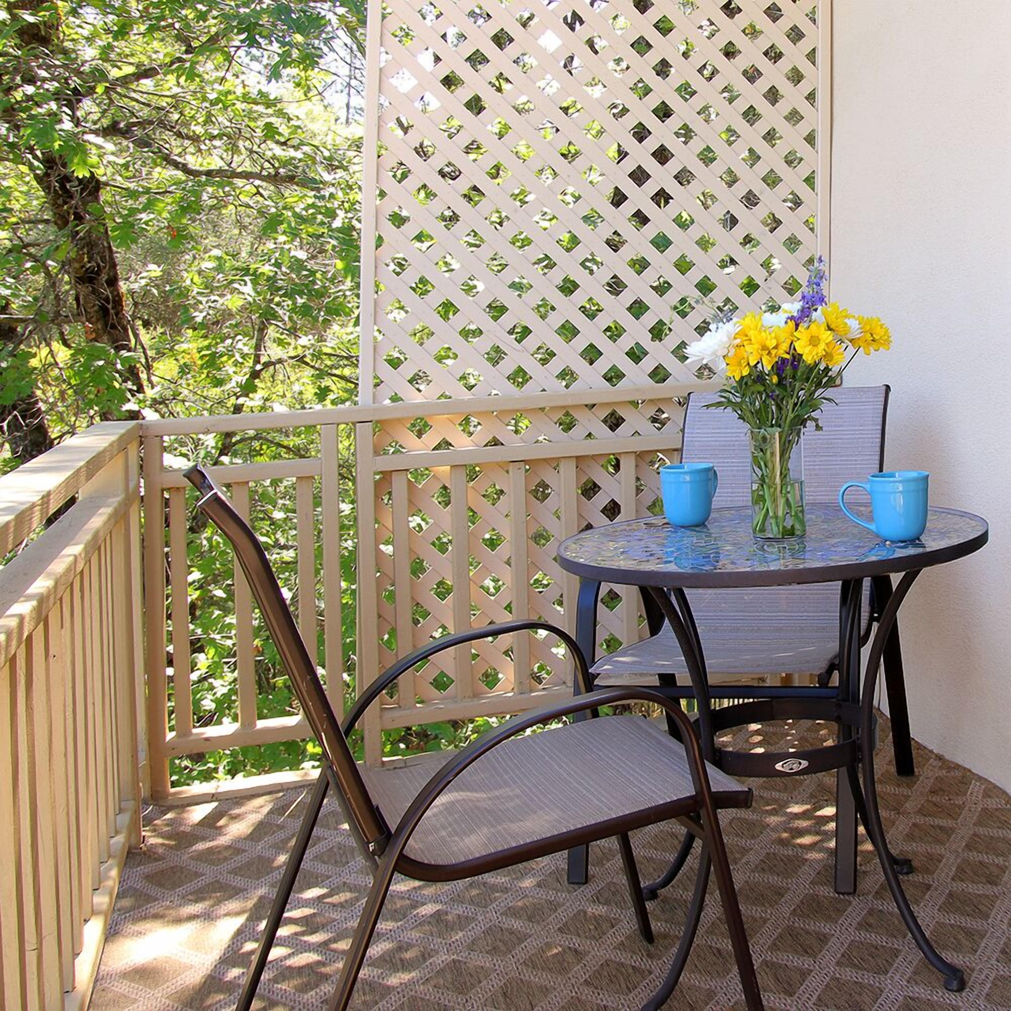 A balcony with a table, chairs, and a vase of flowers.
