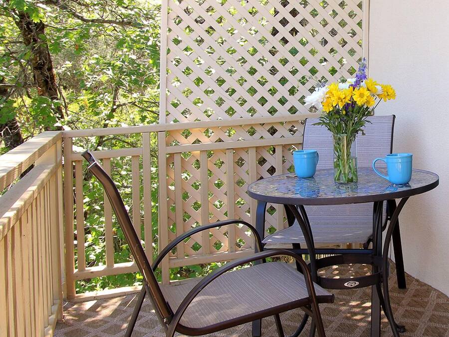 A balcony with a table, chairs, and a vase of flowers.