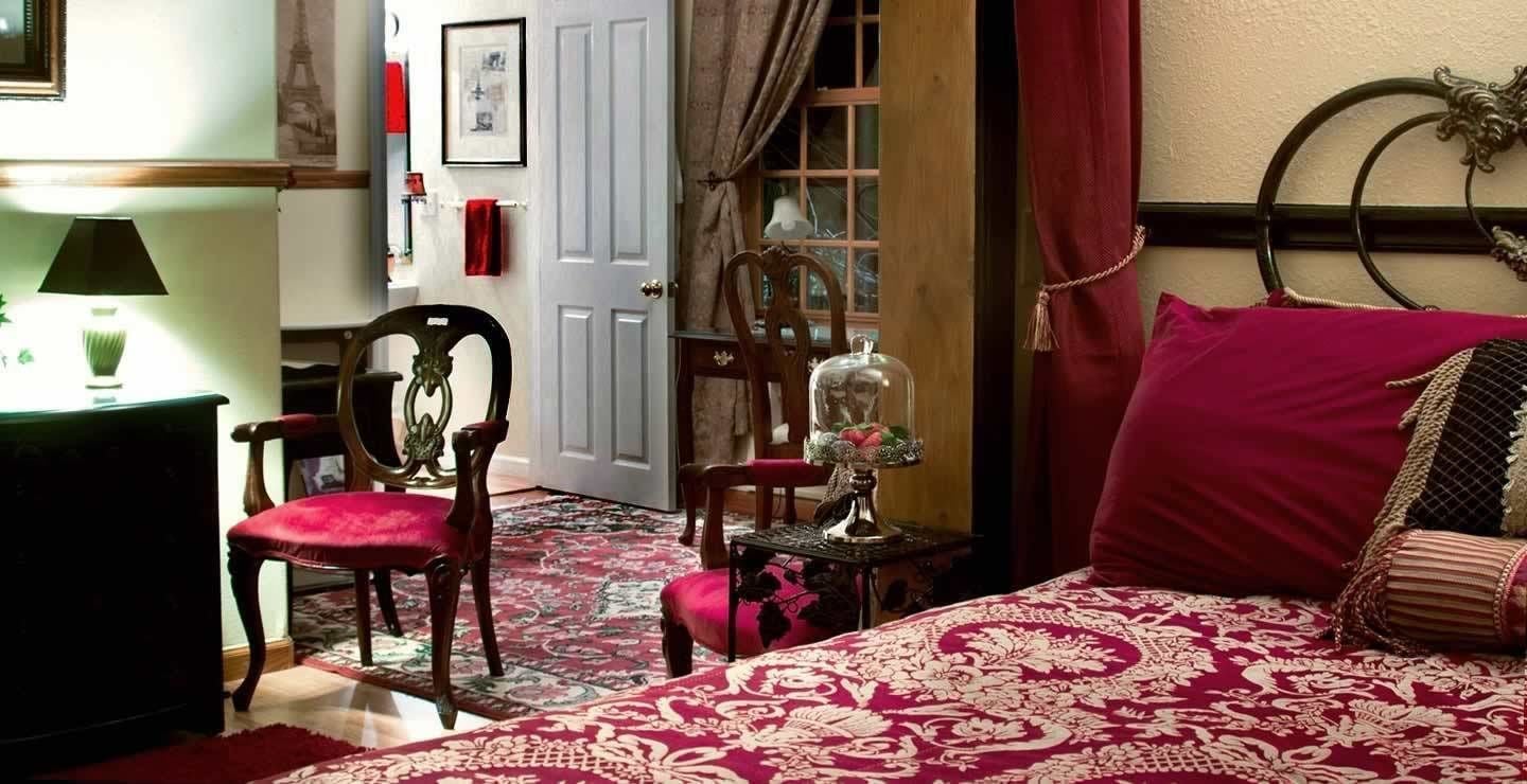 A bedroom with a bed, two chairs, a table with a lamp, and a door.