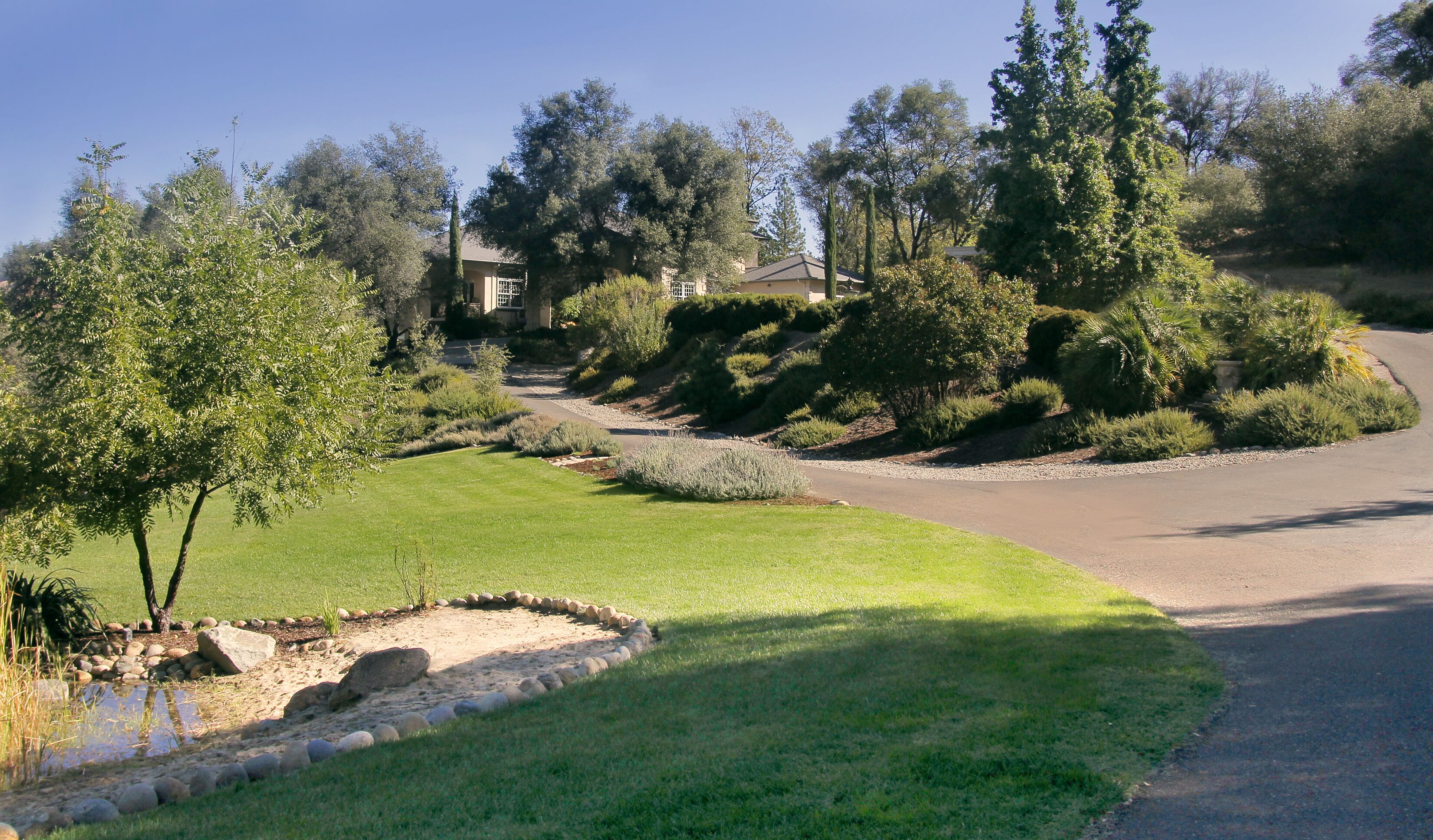 A residential driveway with a landscaped garden, a small pond, and a house in the background.