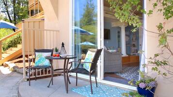 Eine Terrasses mit Korbstühlen, einem kleinen Tisch und einem blauen Teppich mit Muster.