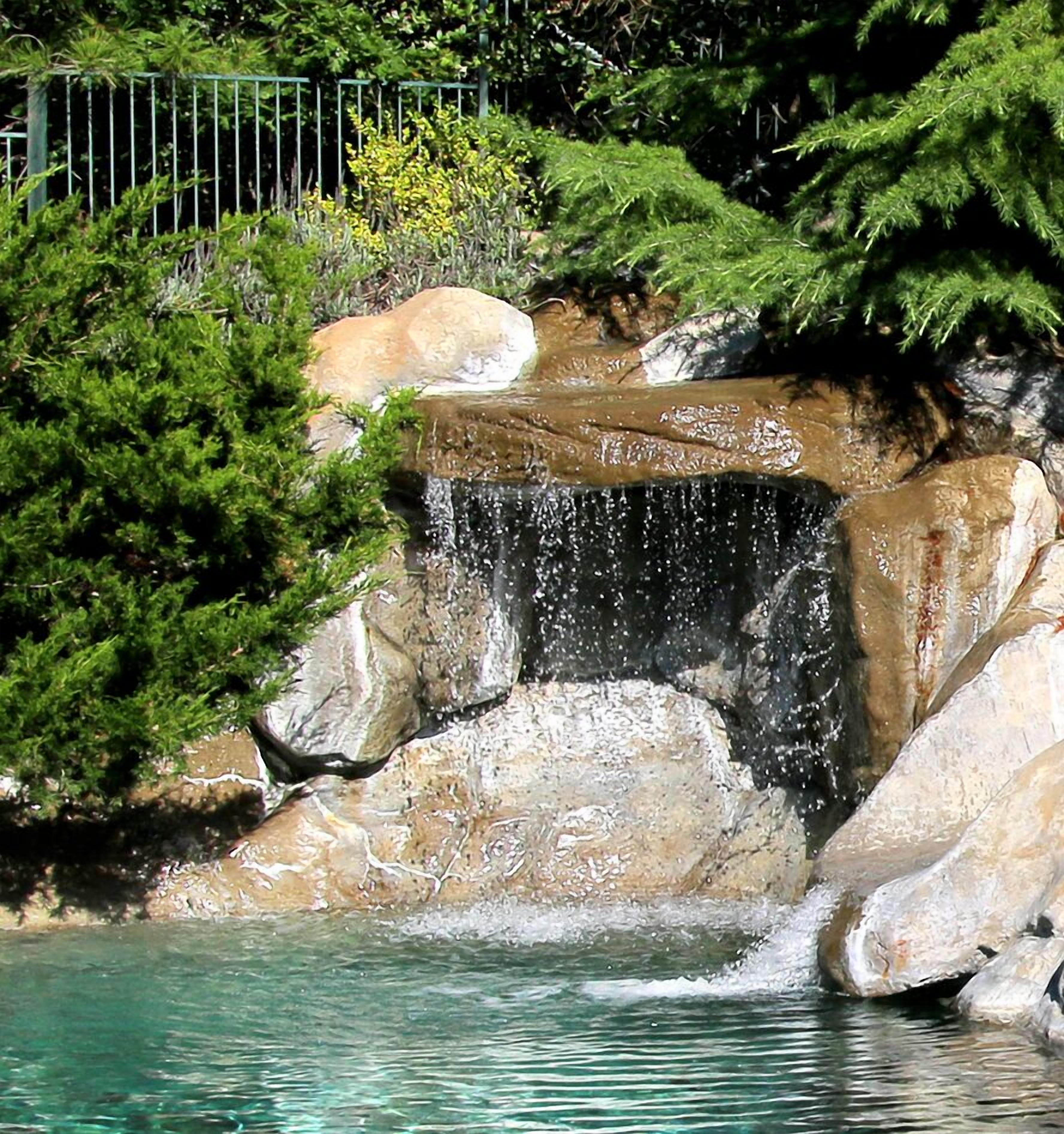 A waterfall feature with clear water, surrounded by rocks and lush greenery.