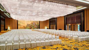 A conference room with rows of white chairs, a large chandelier, and a detailed mural on the back wall.