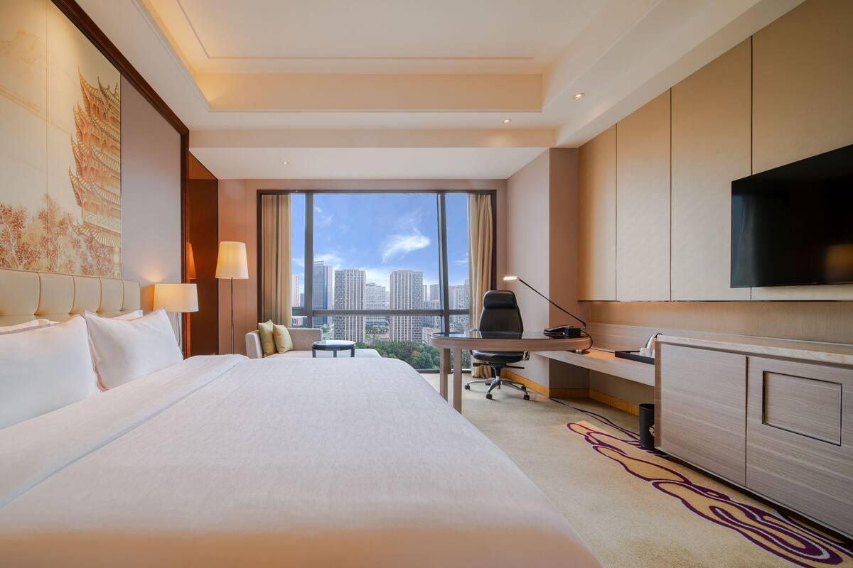 Habitación de hotel con una cama grande, un escritorio con silla, televisión y vistas a la ciudad.