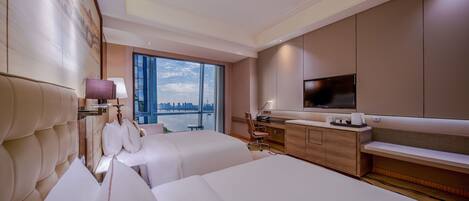 Habitación de hotel con dos camas, un escritorio, un televisor y vistas a un horizonte urbano.