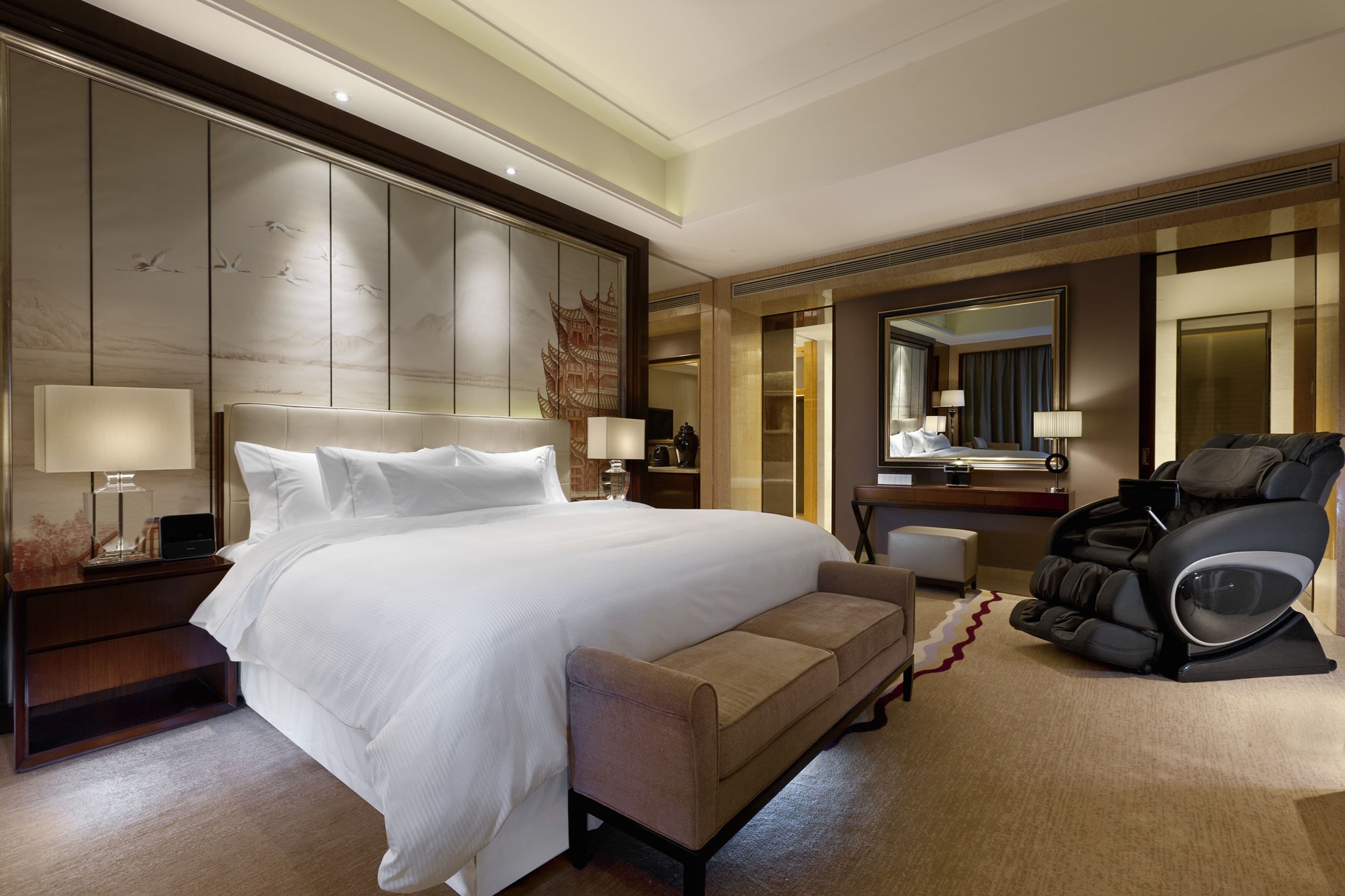 Una habitación de hotel con una cama grande, una silla de masajes, un escritorio y un espejo.