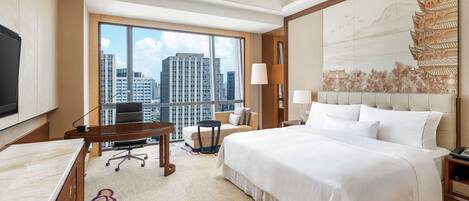 A hotel room with a large bed, a desk, a chair, a sofa, a TV, and a large window with a city view.