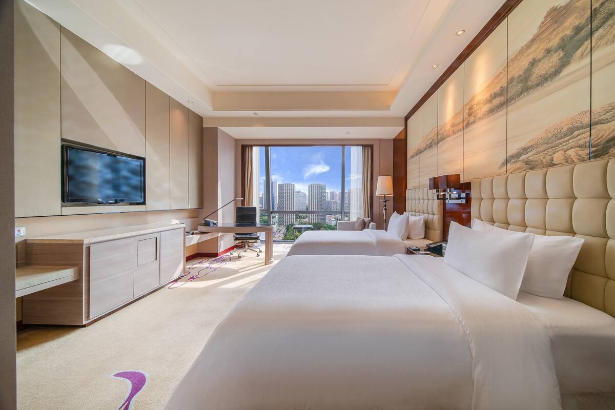 Habitación de hotel con una cama grande, un escritorio, un televisor y vistas a la ciudad.