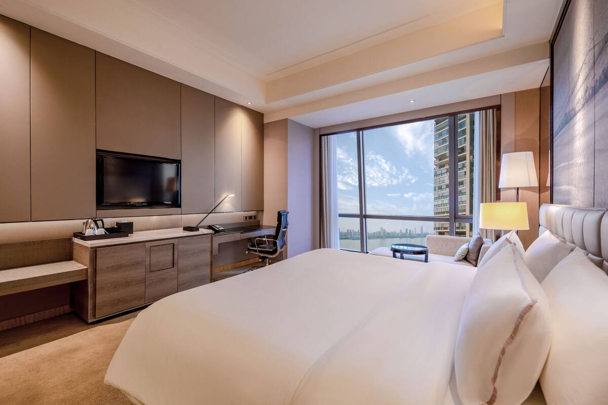 Una habitación de hotel moderna con una cama grande, un escritorio, un televisor y vistas de la ciudad.