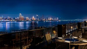 Un restaurant situé au bord de l’eau, avec des tables dressées pour le dîner, offrant une vue sur les lumières de la ville la nuit.