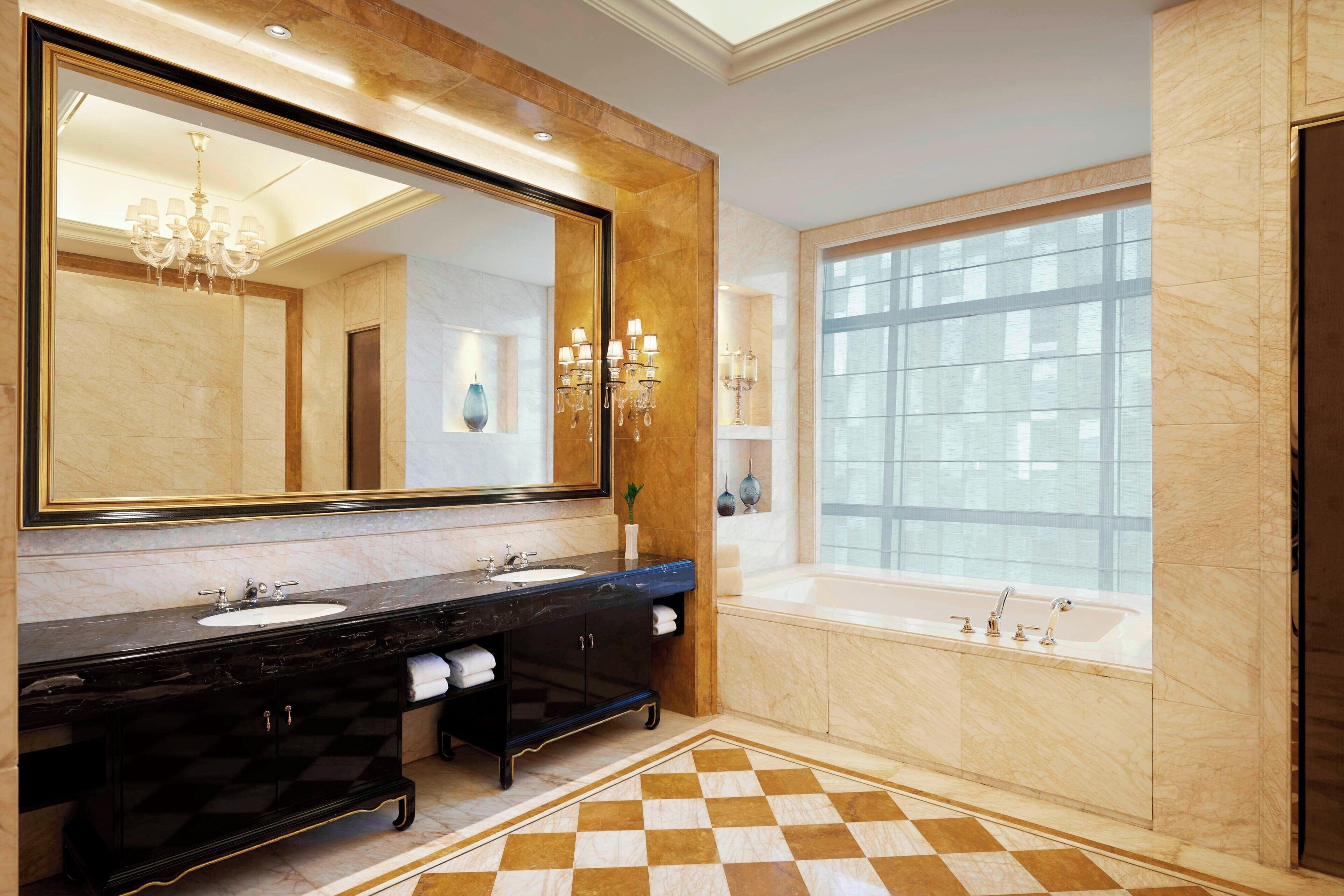 Une salle de bain luxueuse avec un grand miroir, deux vasques, une baignoire et un carrelage à motifs géométriques.