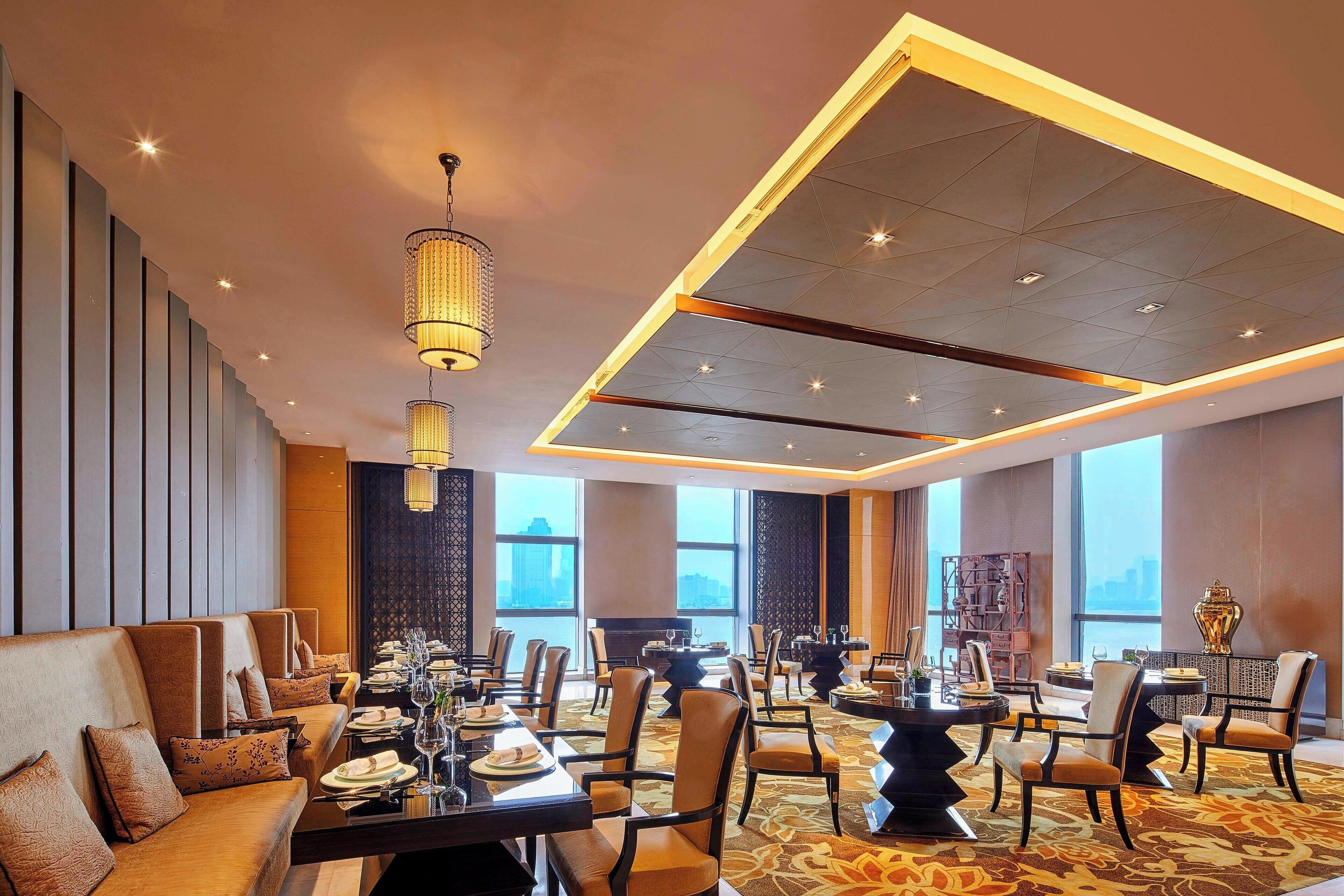 A modern dining area with high ceilings, ambient lighting, and a view of the cityscape through large windows.